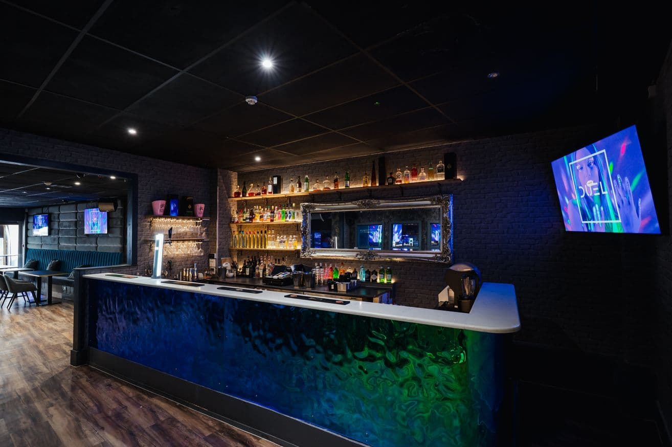 Room 2 at DUEL, its bar lit blue and green beside the seating